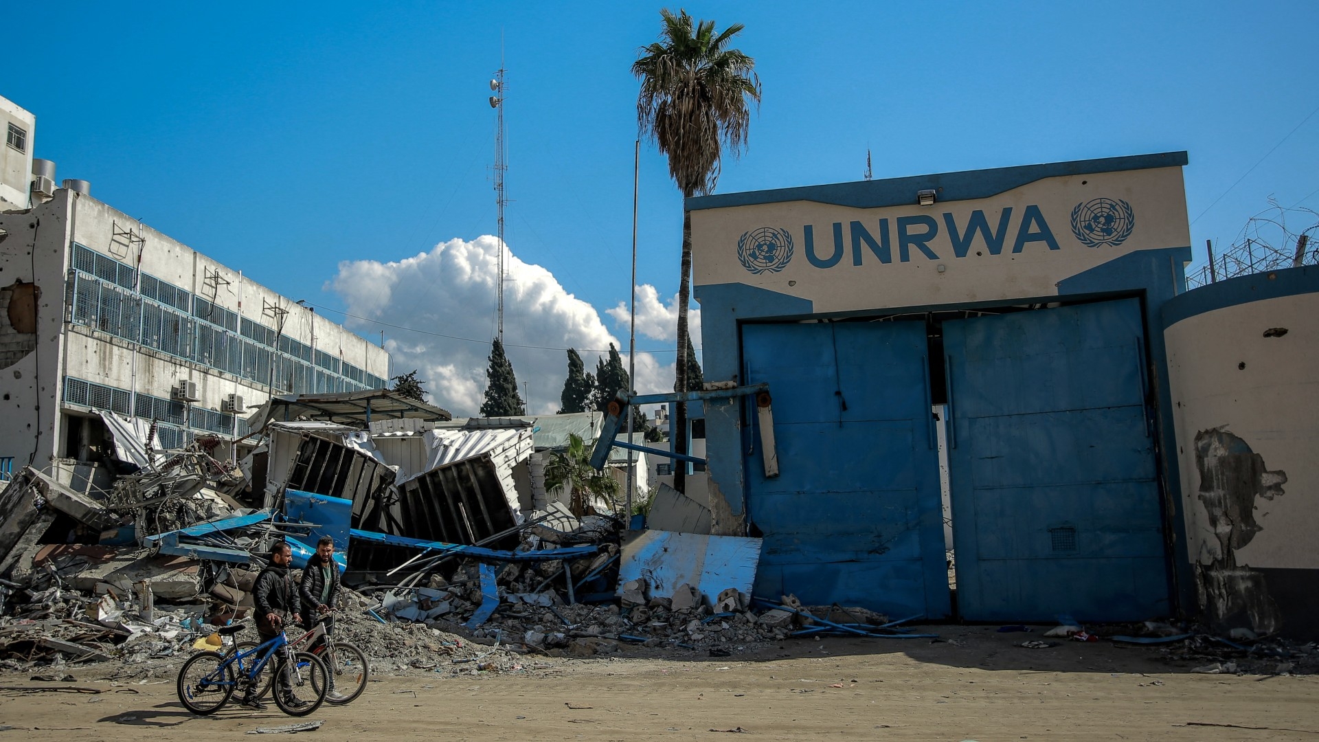 People walk past the damaged Gaza City headquarters of the United Nations Relief and Works Agency for Palestine Refugees (Unrwa) on 15 February 2024 (AFP)