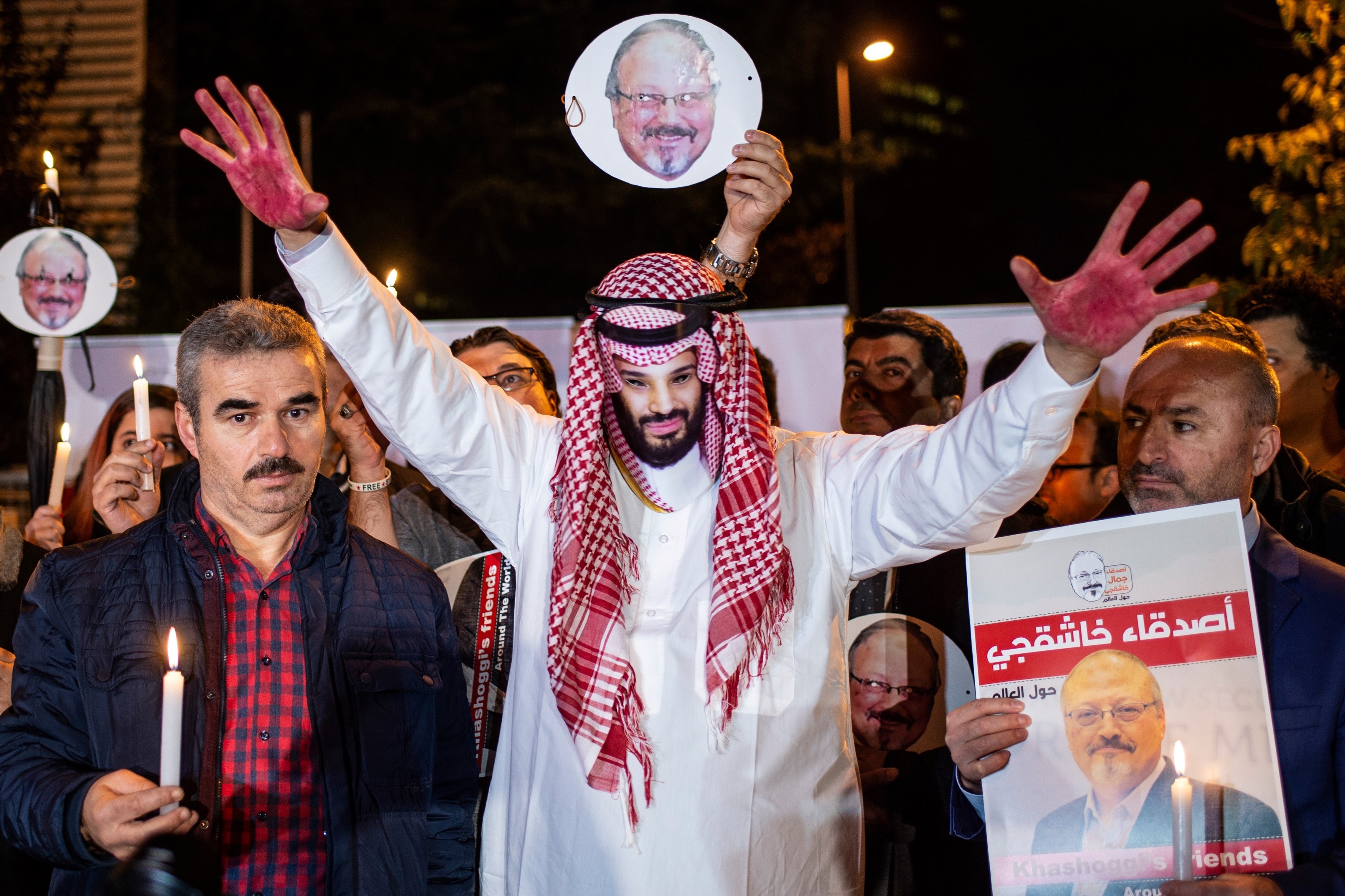 A protestor wears a mask of depicting Saudi Crown Prince Mohammad Bin Salman with red painted hands next to people holding posters of Saudi journalist Jamal Khashoggi during the demonstration outside the Saudi Arabia consulate in Istanbul, on 25 October, 2018 (AFP)