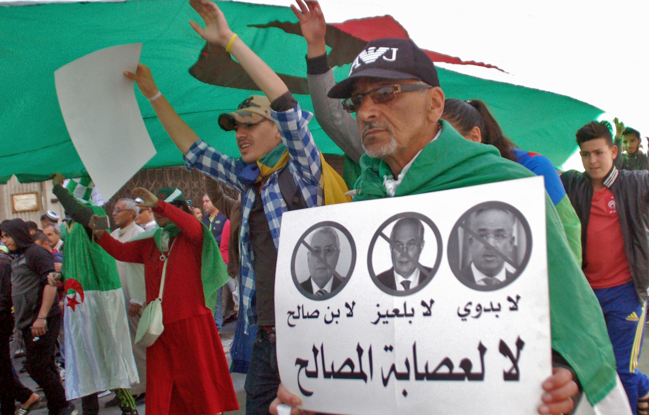 An Algerian man marches with a sign against the "3B" (Interim leader Abdelakder Bensalah, constitutional council chief Tayeb Belaiz and Prime Minister Noureddine Bedoui)in the city of Oran on 9 April (AFP)