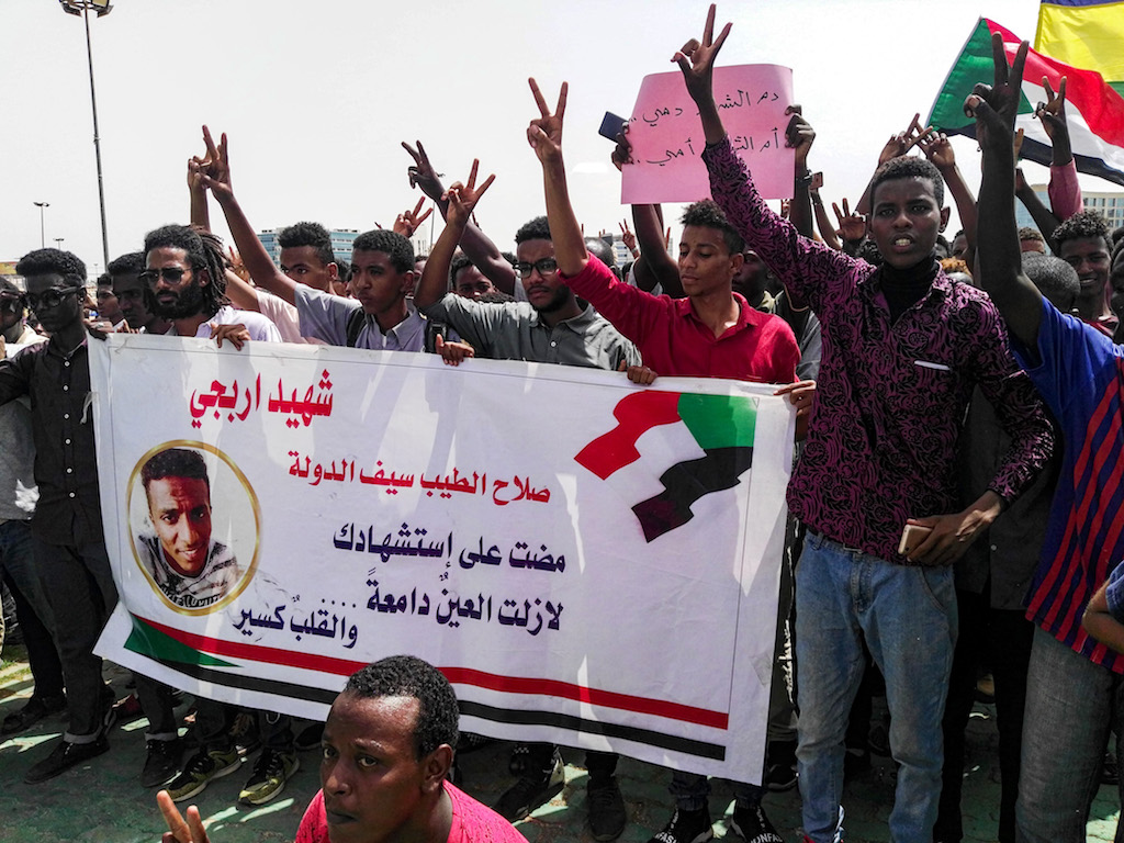 Sudanese protesters chant slogans and wave national flags as they stand behind a banner showing the name of a killed protester during a demonstration in the capital Khartoum's Green Square 