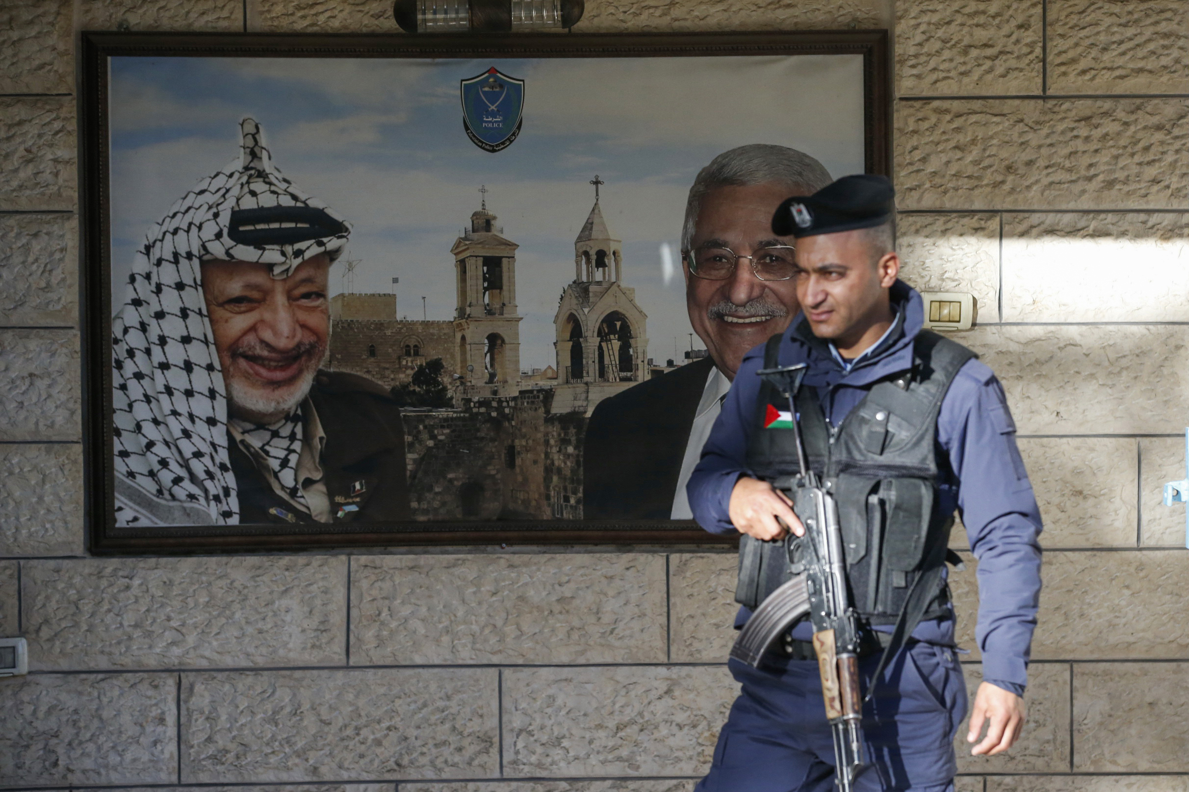   A Palestinian policeman stands guard in front of a poster bearing the portraits of late Palestinian leader Yasser Arafat (L) and Palestinian president Mahmoud Abbas at the Church of the Nativity on 24 December, 2019 (AFP)