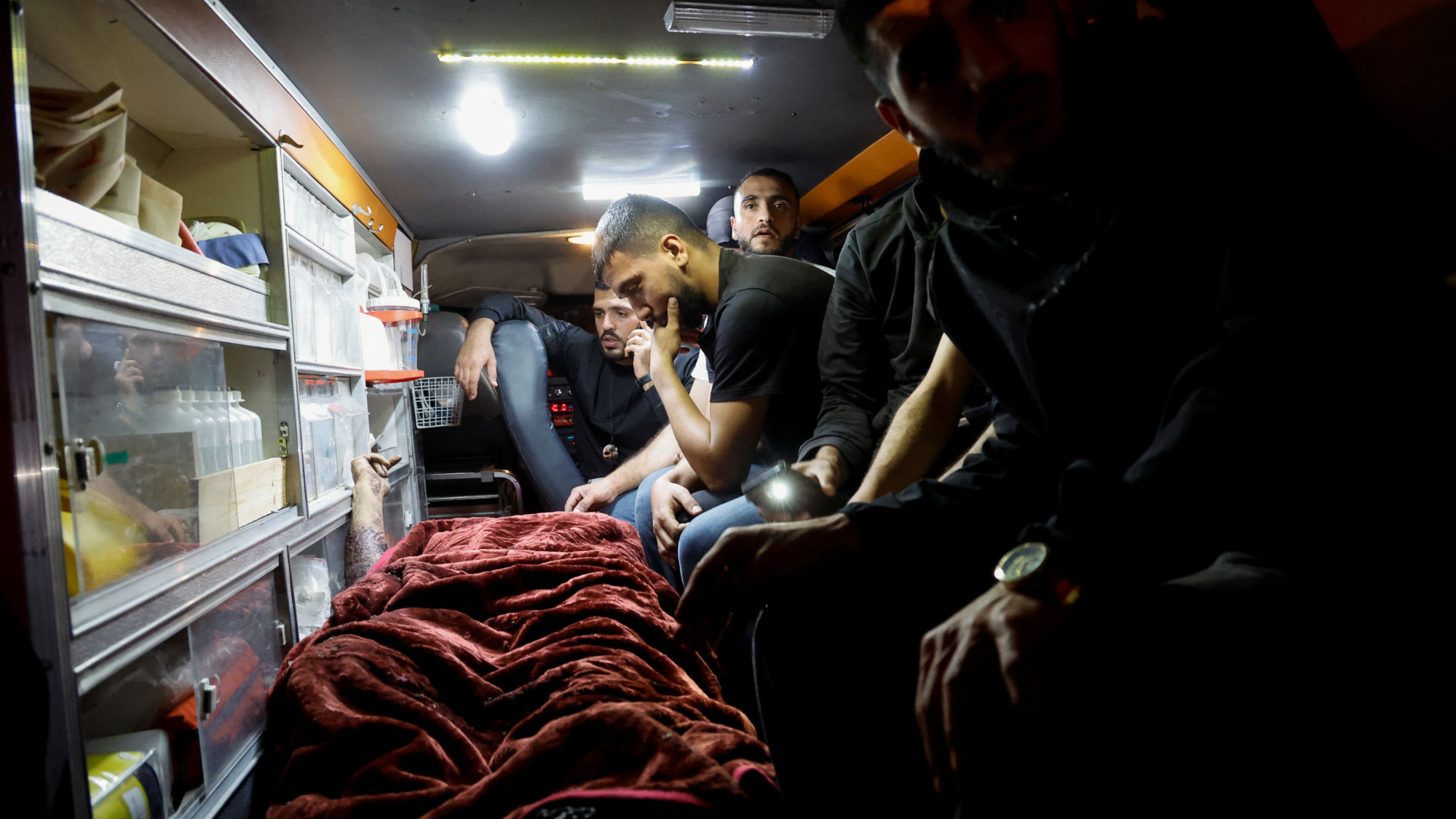 Palestinians sit in an ambulance, next to the body of a man who was killed in an Israeli raid at Nur Shams camp, Tulkarm, in the occupied West Bank, 20 April 2024 (Reuters/Raneen Sawafta)