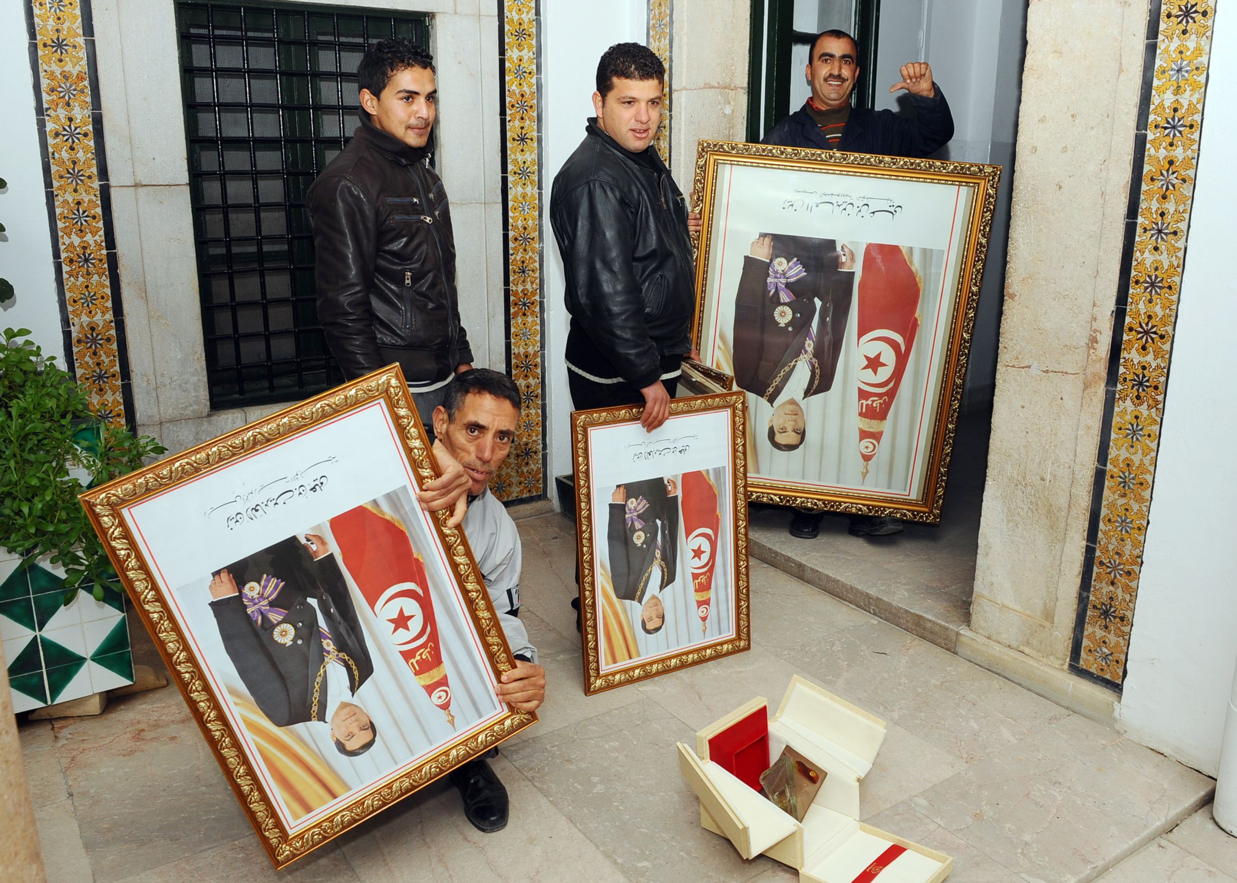 Tunisian employees of the Prime ministry remove portraits of Ben Ali on 17 January 2011, three days after he fled the country following a month of protests (AFP)