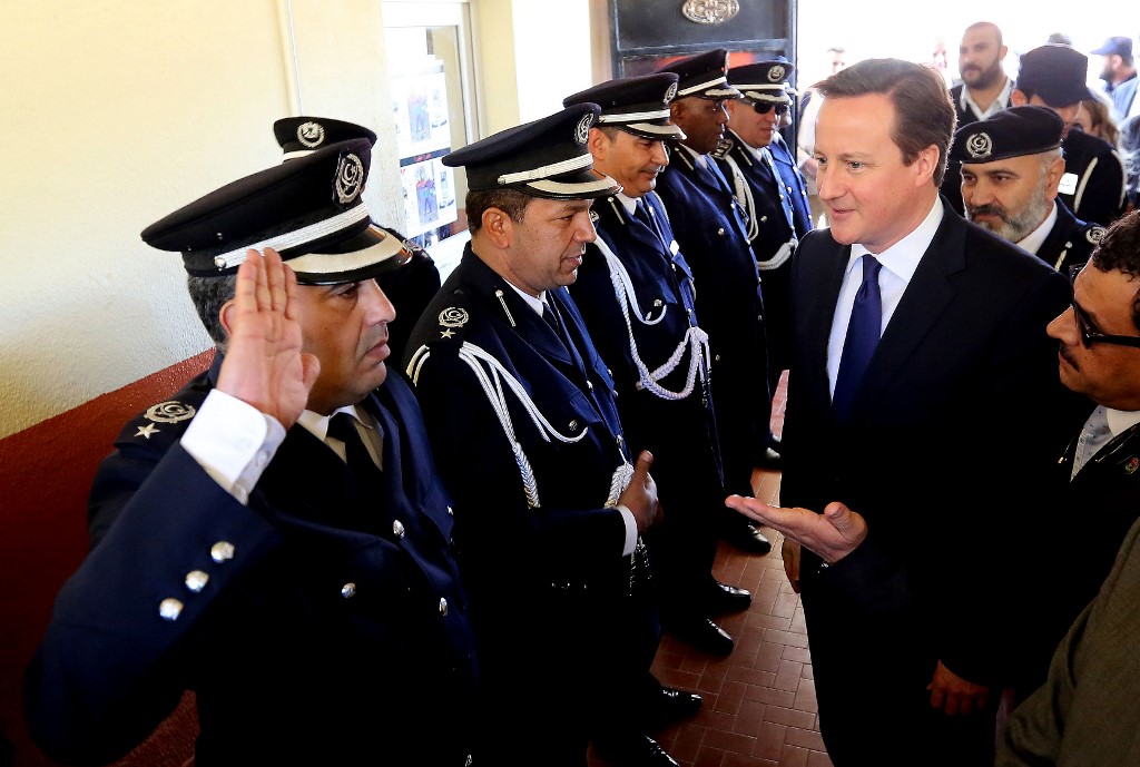 A Libyan police officer salutes Cameron in Tripoli in 2013 (AFP)