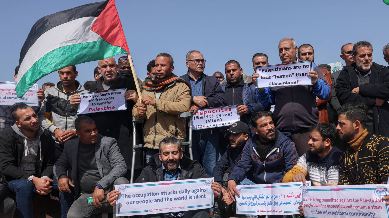 Palestinians lift placards during a rally demanding international support for Palestinians against Israel, similar to that shown for Ukrainians against Russia, in Gaza on 5 March 2022 (AFP)