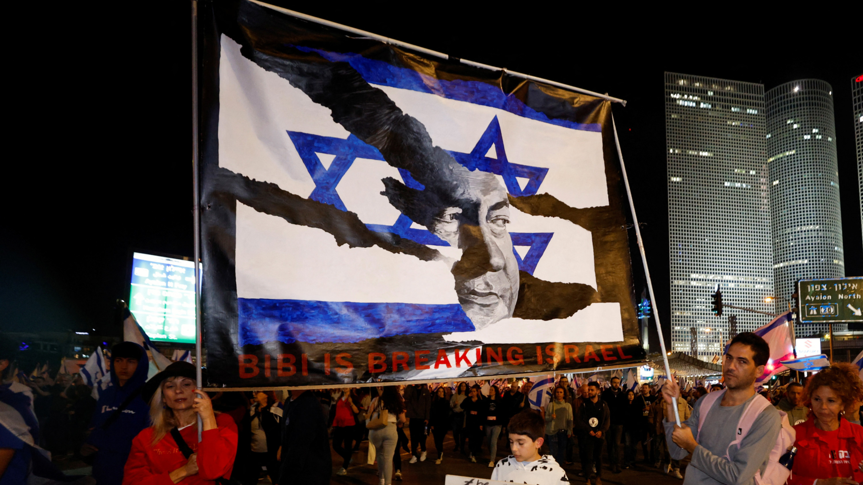 Protestors holding a banner in Tel Aviv as Israeli Prime Minister Benjamin Netanyahu's nationalist coalition government presses on with its judicial overhaul, 25 March 2023 (AFP).jpg
