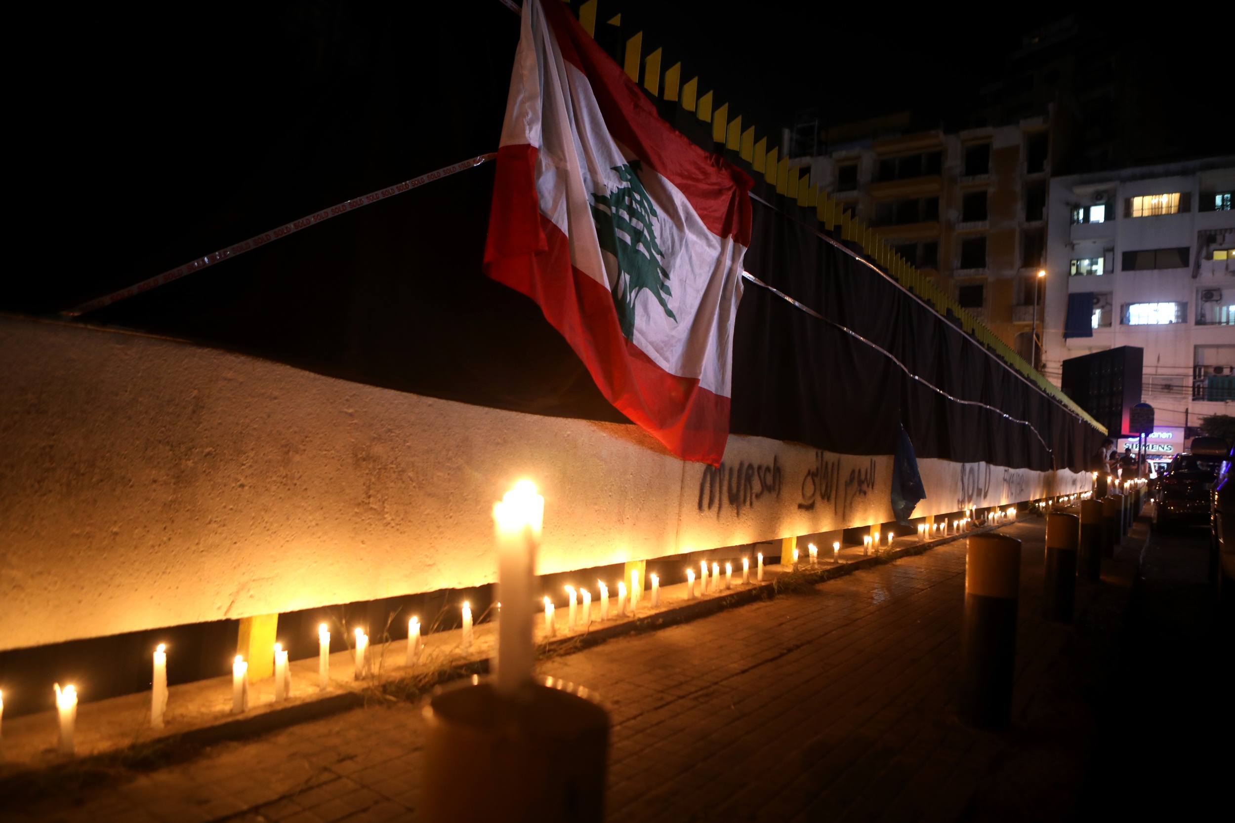 The Lebanese flag hangs on the walls of the electricity company headquarters covered with black fabrics as protesters take part in a candle light vigil in Beirut on 11 November 2019 (AFP)