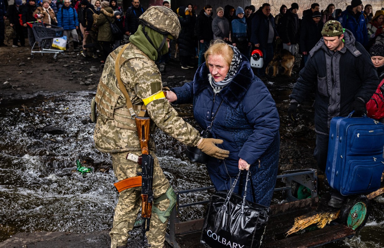 A Ukrainian serviceman helps evacuees gathered under a destroyed bridge, as they flee the city of Irpin, northwest of Kyiv, on 7 March 2022 (AFP)