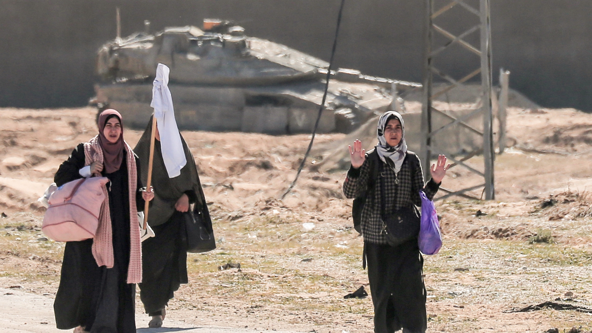 Displaced Palestinian women carrying their belongings lift a makeshift white flag as they walk past Israeli forces while fleeing the Hamad City area in Khan Yunis in the southern Gaza Strip on 5 March (AFP)