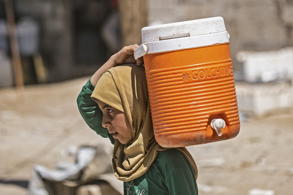A displaced Syrian girl carries water on her shoulder in al-Hol camp on 18 April (AFP)