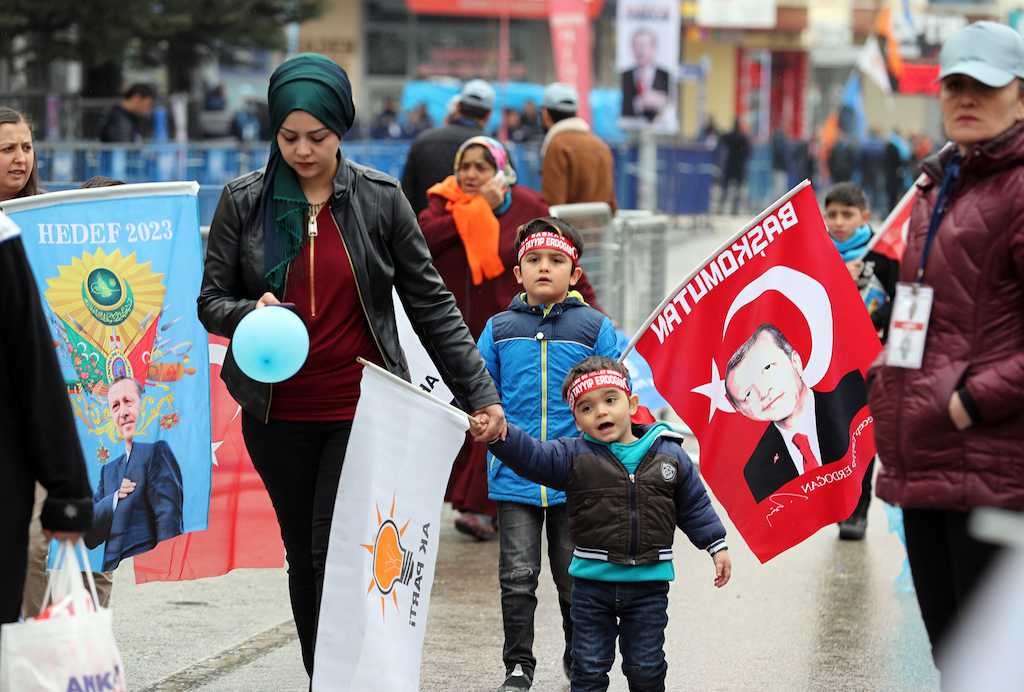 A woman walks with her child as people gather to listen to Turkish President Recep Tayyip Erdogan during a campaign rally of the Turkey's ruling party in Ankara (AFP)