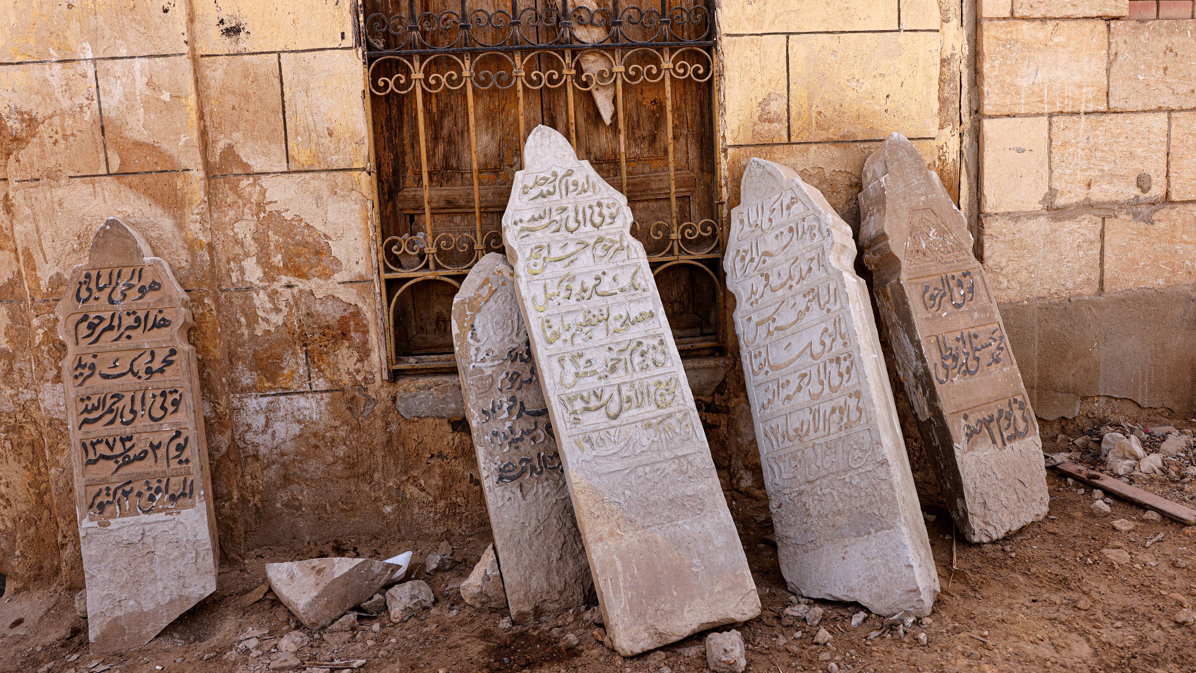 Graves carved with Arabic calligraphy lay on the side of a brick building.