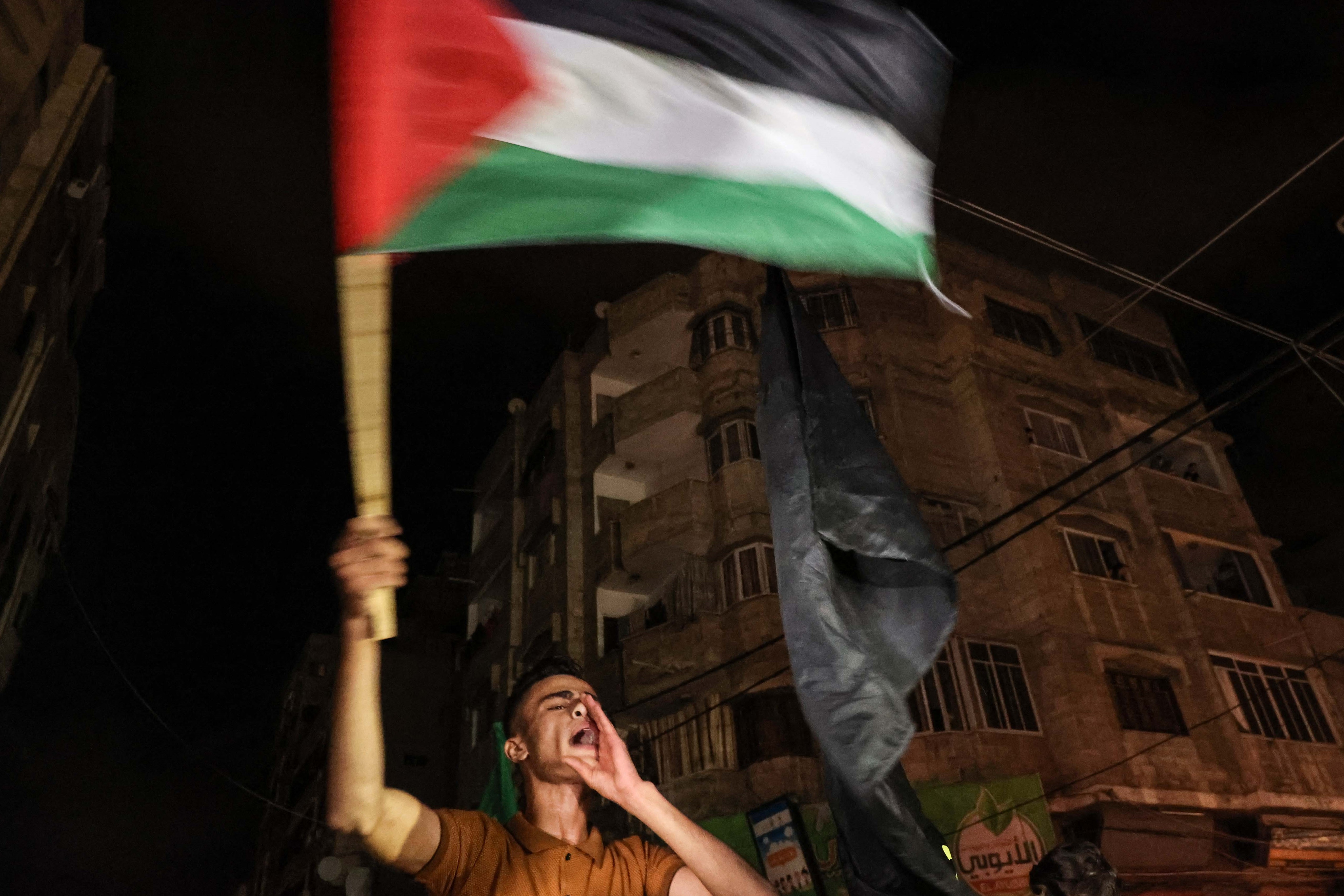 A man waves the Palestinian flag as people celebrate the ceasefire brokered by Egypt between Israel and the two main Palestinian armed groups in Gaza City on May 21, 2021.