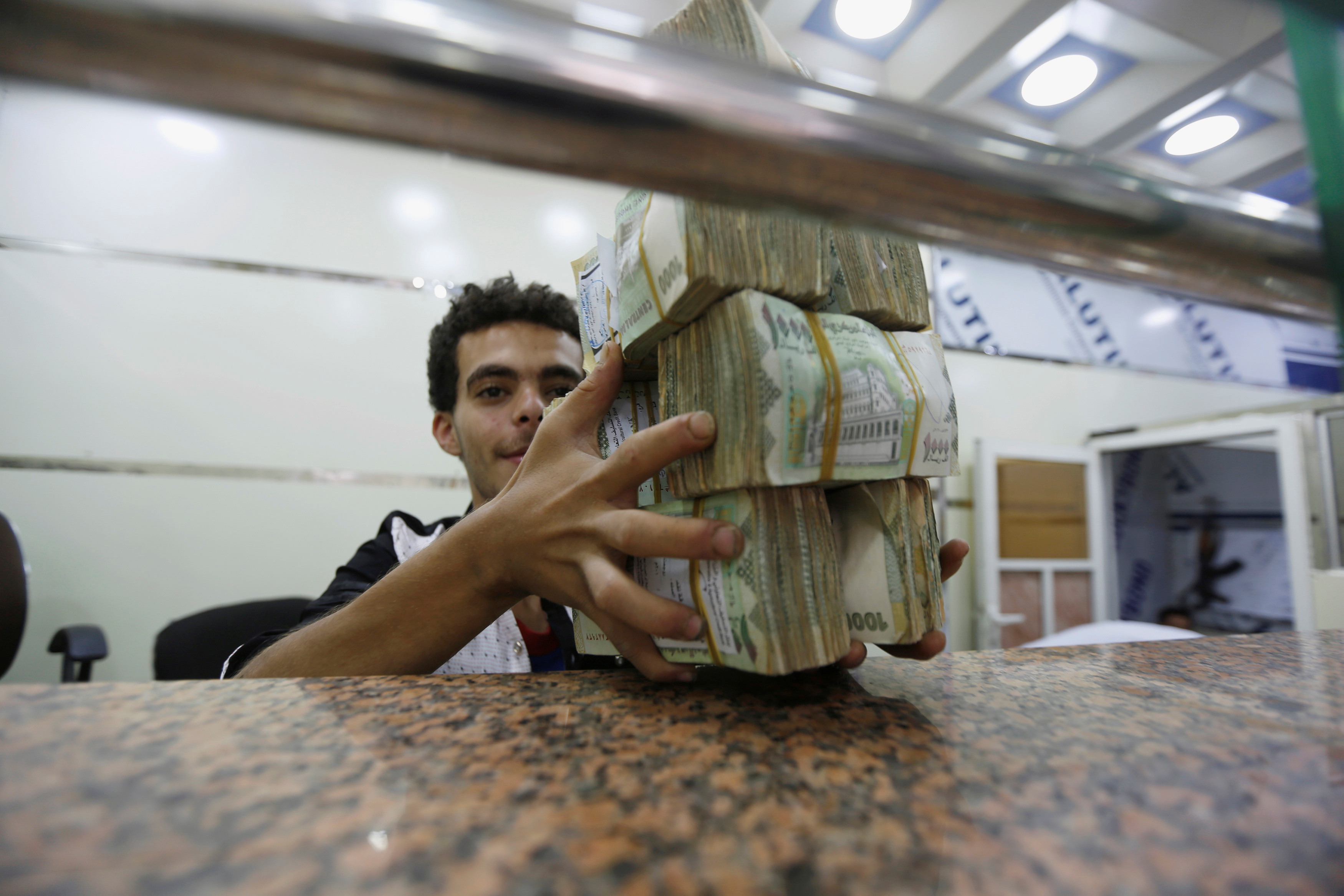 A money changer holds bundles of Yemeni currency at an exchange shop in Sanaa (Reuters)