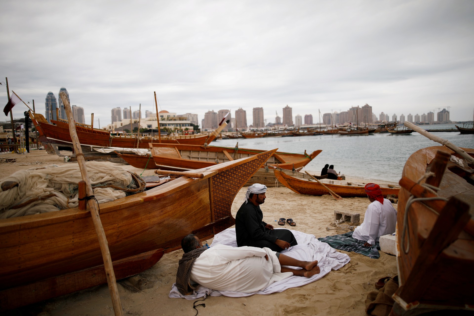 Men rest between wooden boats on Katara beach in Doha in 2019 (Reuters)