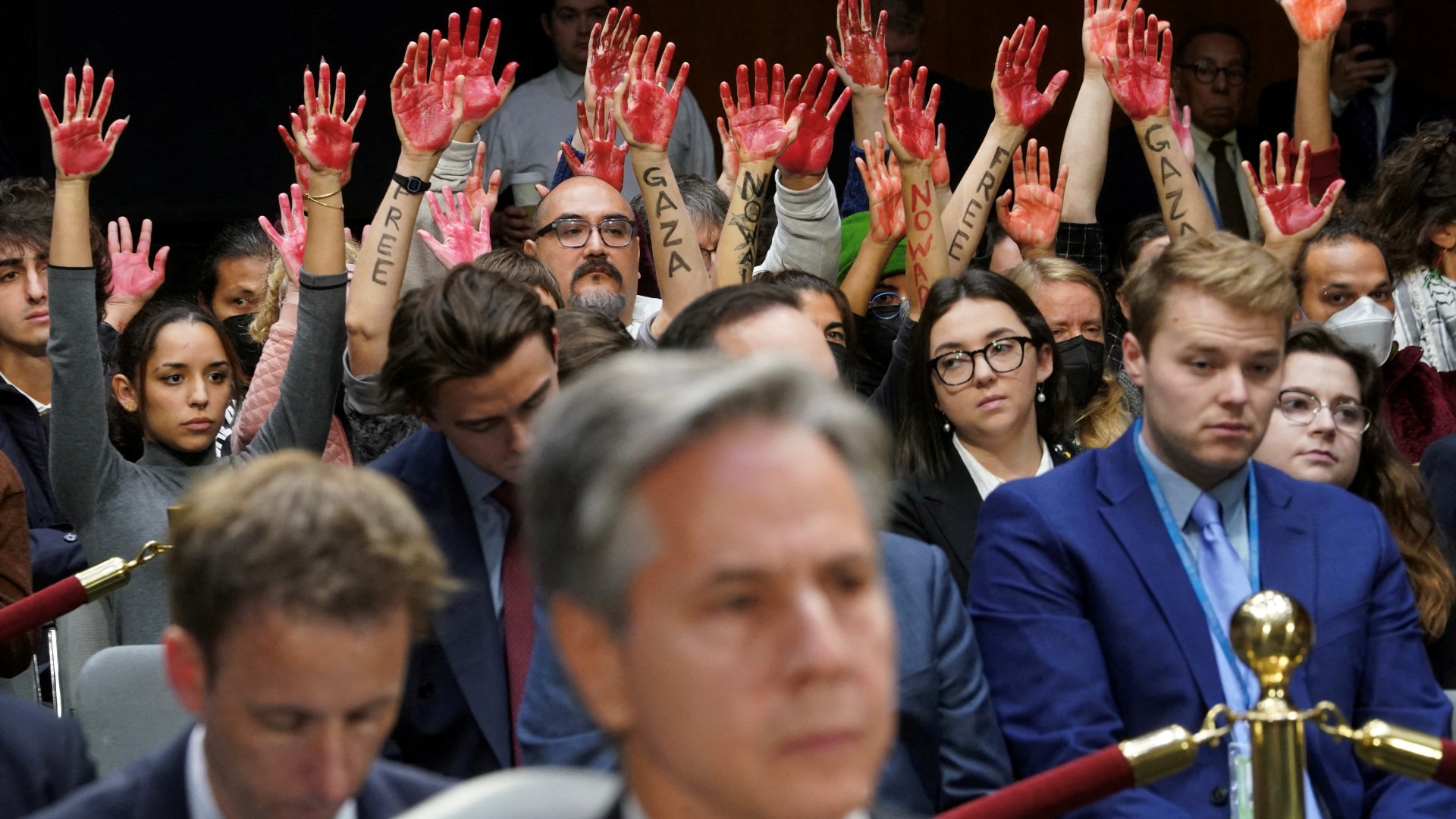 Anti-war protesters raise their "bloody" hands behind US Secretary of State Antony Blinken during a Senate Appropriations Committee hearing on 31 October (Reuters)