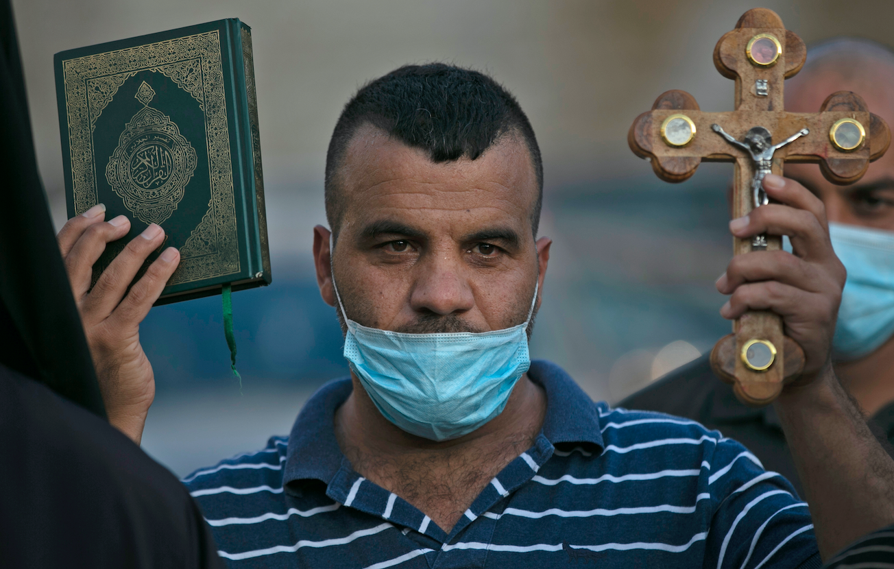 Un Palestinien tient une croix et un Coran lors d’une manifestation contre les propos du président Emmanuel Macron sur les caricatures du prophète Mohammed, à Bethléem, le 28 octobre 2020 (AFP)