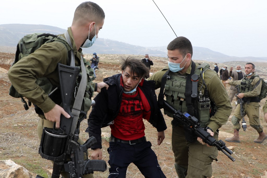 Israeli soldiers detain a Palestinian man during a protest against the seizure of Palestinian farmland by Jewish settlers in the occupied West Bank on 13 January 2021 (AFP)