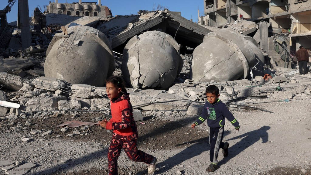 Palestinian children walk past the rubble of a mosque after an Israeli air strike in the southern Gaza Strip on 22 February 2024 (Said Khatib/AFP)