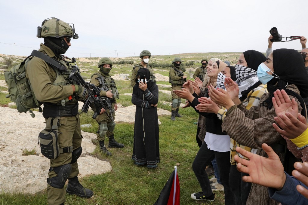 Palestinian women chant slogans as Israeli soldiers stand guard during a protest in the Palestinian village of Susya in the occupied West Bank on 14 March 2021 (AFP)