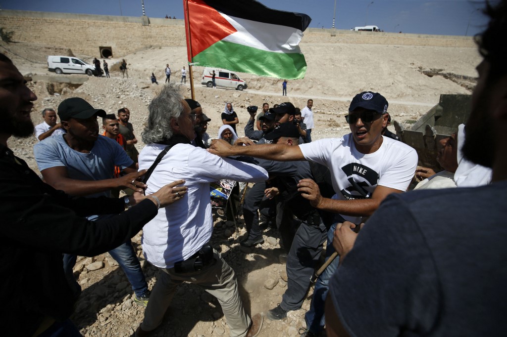 Israeli forces scuffle with American-French law professor Frank Romano (white shirt L) and other Palestinian protestors, with a Palestinian national flag in the background, on September 14, 2018,