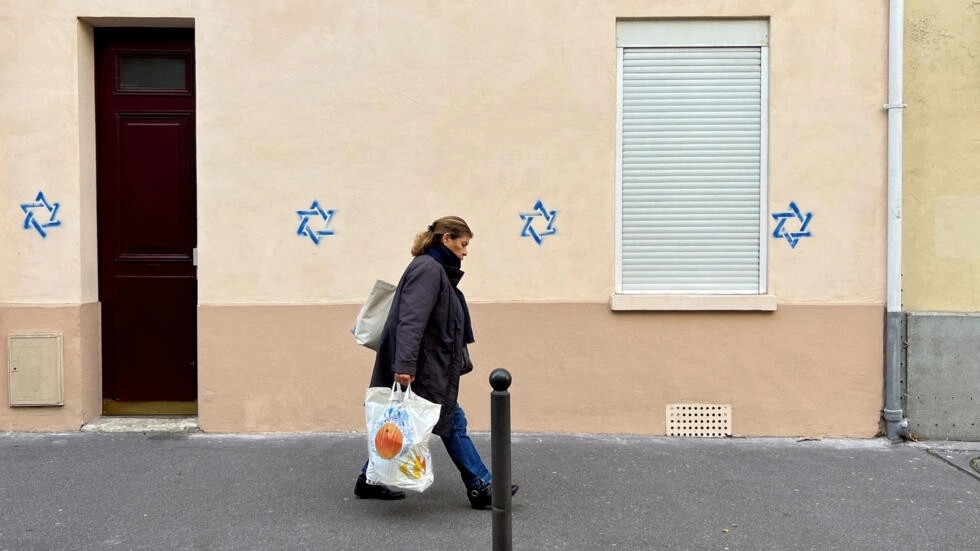 A woman walks past a building tagged with Stars of David in Paris, France, 31 October 2023 (Reuters)