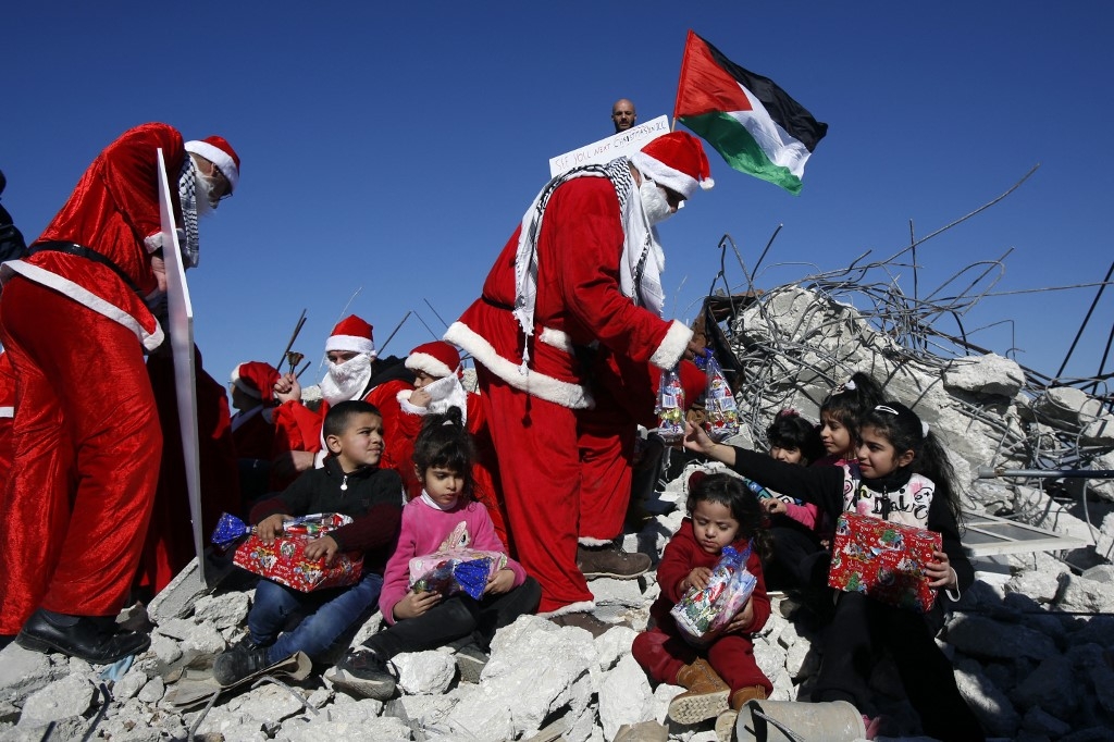'As ever, one is struck by the sheer resilience of the Palestinian people.' Palestinians wearing Christmas costumes give gifts to children in the rubble of a house in the occupied West Bank demolished by Israel, 23 December 2019 (AFP)