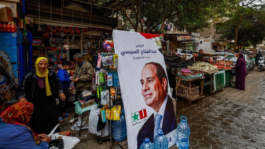 People walk past a campaign poster of Egypt's President Abdel Fattah al-Sisi in a market in Cairo on 7 December 2023, ahead of the presidential election (AFP)