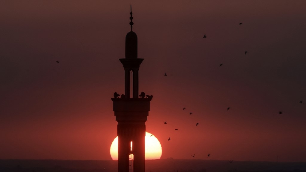 The sun sets behind the minaret of a mosque in Rafah in the southern Gaza Strip on 29 December 2023 (AFP)