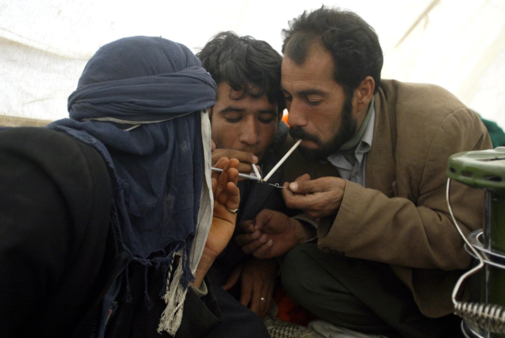Iranian men smoke opium in a tent in the southeastern Iranian city of Bam on 31 December 2003 (AFP)