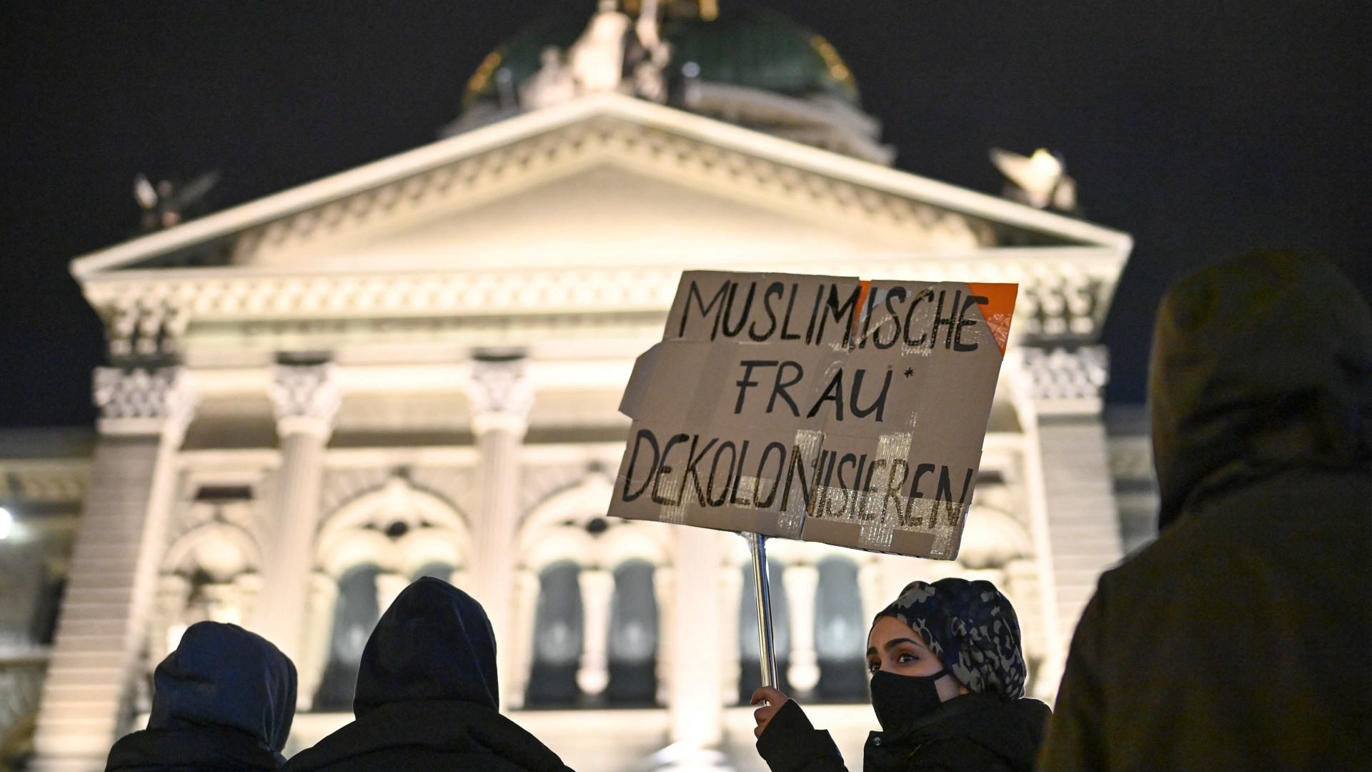 A woman holds a sign that reads, 'Muslim woman decolonize' during a protest following a referendum to ban full facial coverings in public places in Bern, Switzerland on 7 March 2021 (AFP)