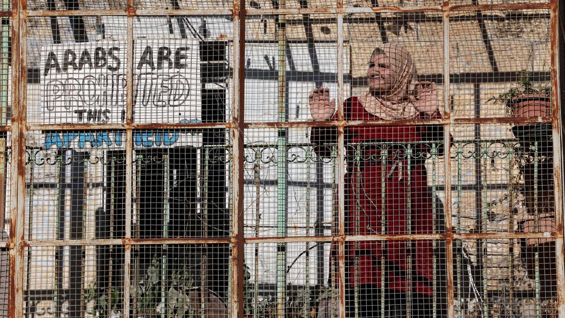 A Palestinian woman stands at a fence separating Jewish settlers from Palestinians in Hebron