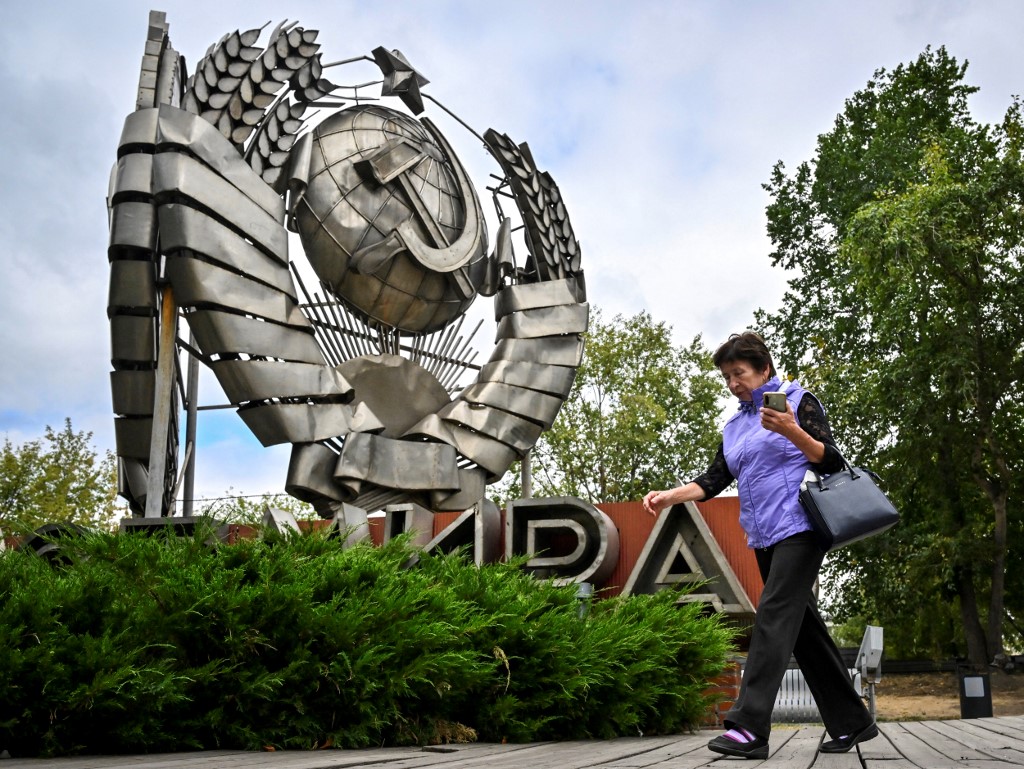 A woman walks past an emblem of the USSR at a sculpture park in Moscow on 31 August 2022 (AFP)